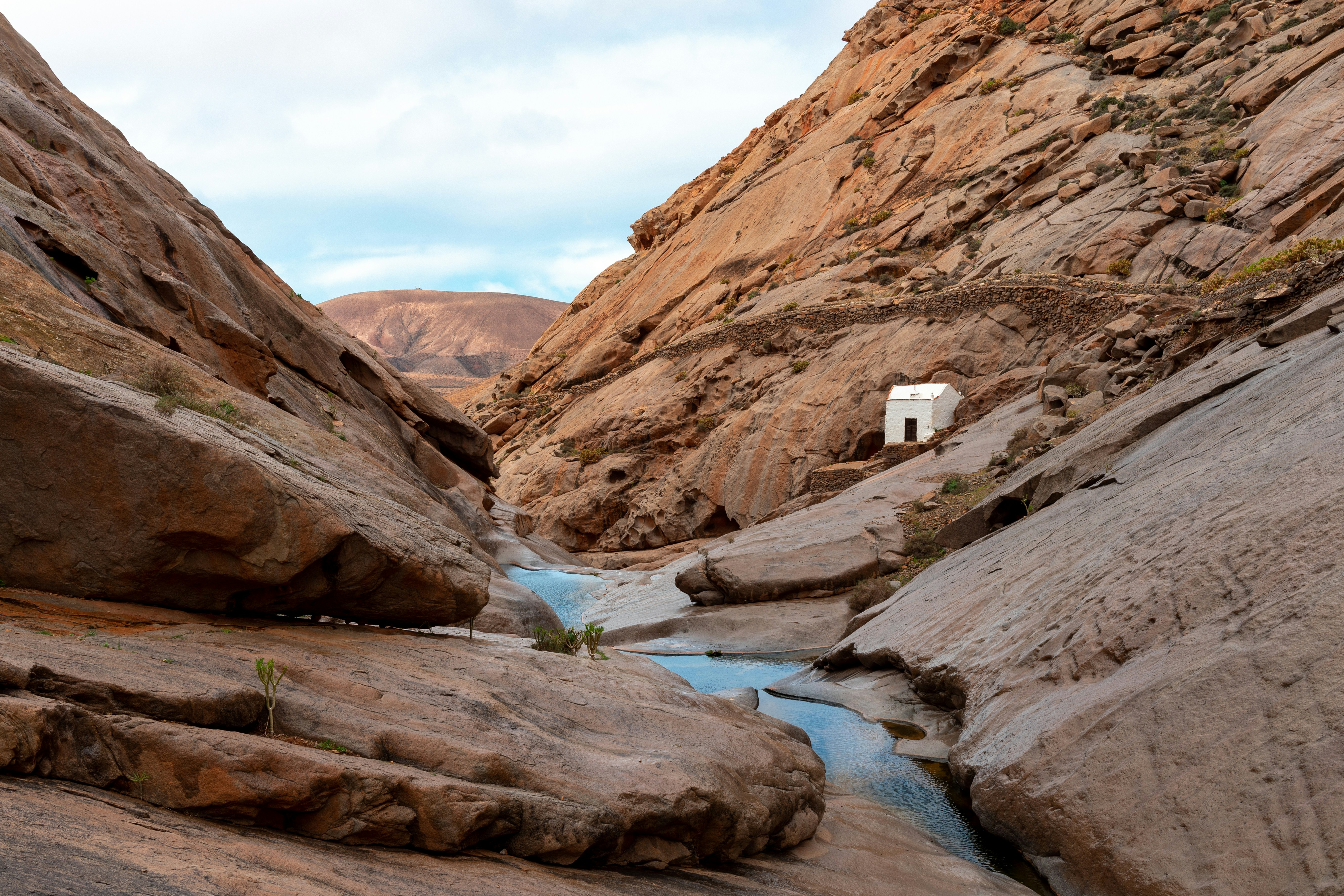 A hidden canyon of sculpted sandstone with a blue water pool leading to a small white chapel nestled between towering rock walls