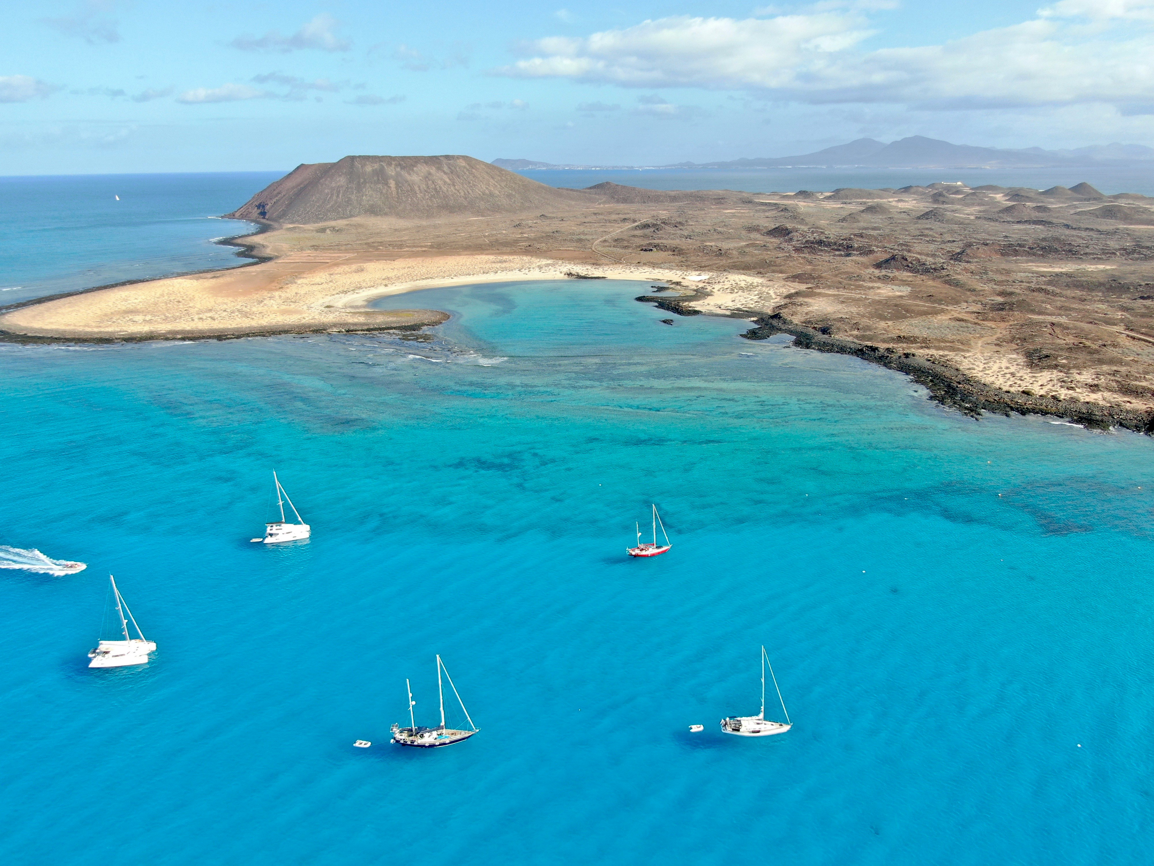 Sailboats anchored in vivid turquoise water off Isla de Lobos with its volcanic crater and sandy lagoon