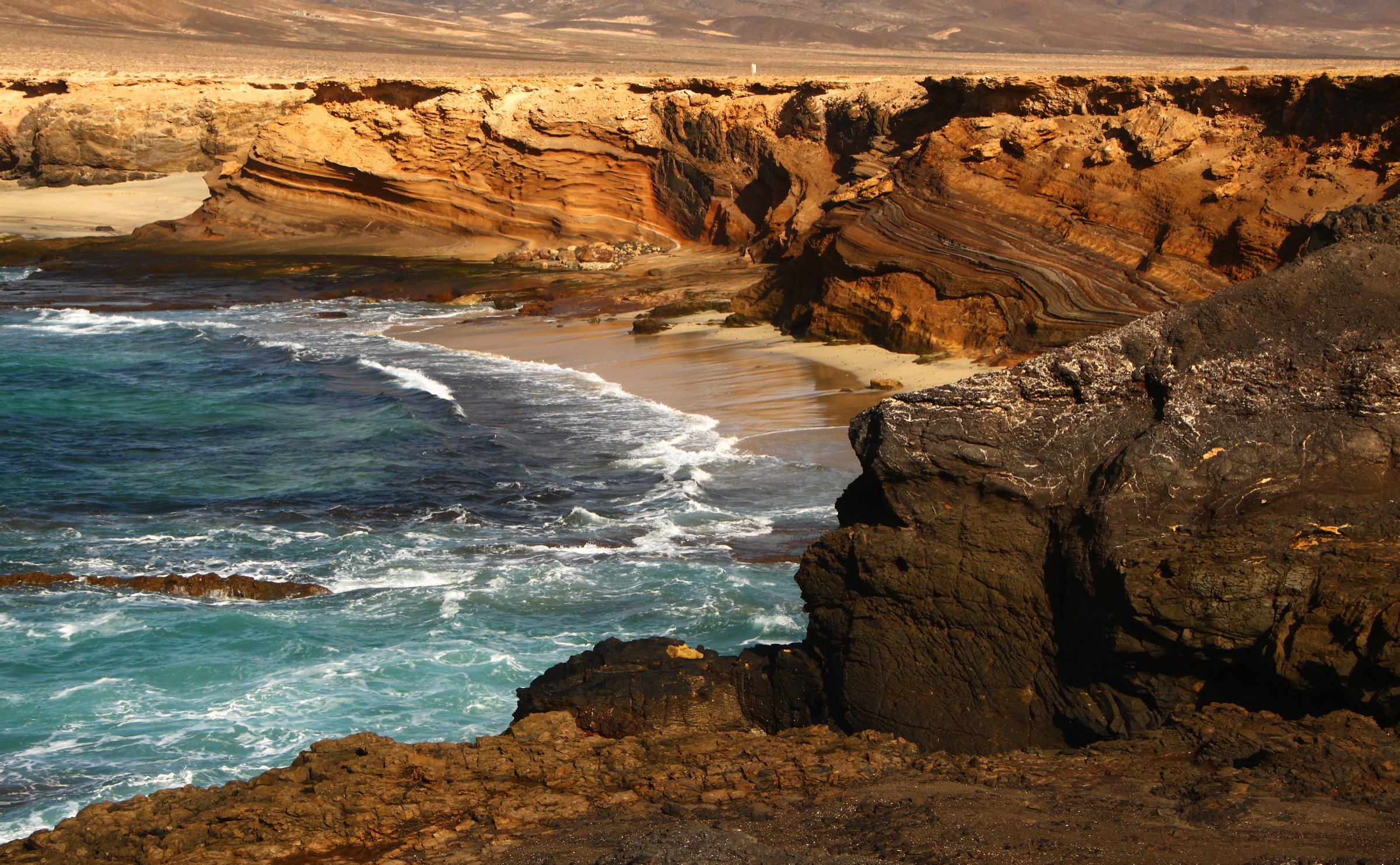 Golden sandstone cliffs meeting turquoise waves at Playa de Ojos