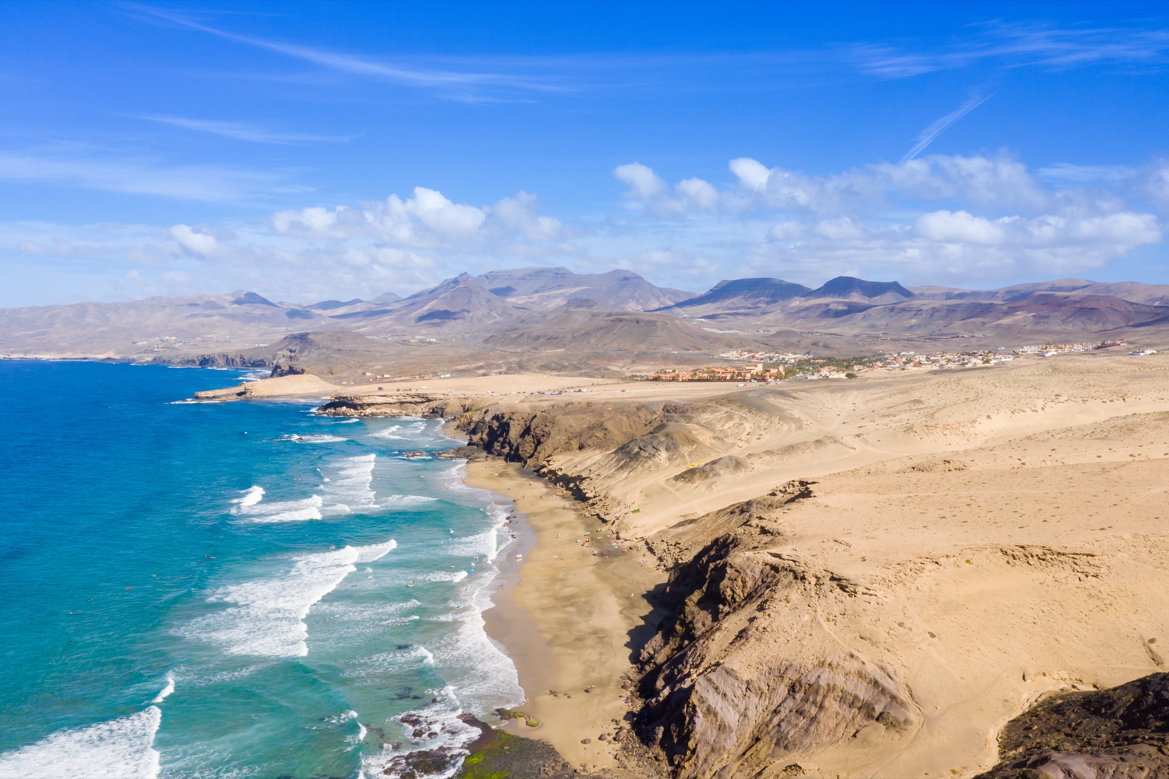 Aerial view of Playa del Viejo Rey with turquoise waves breaking along golden cliffs