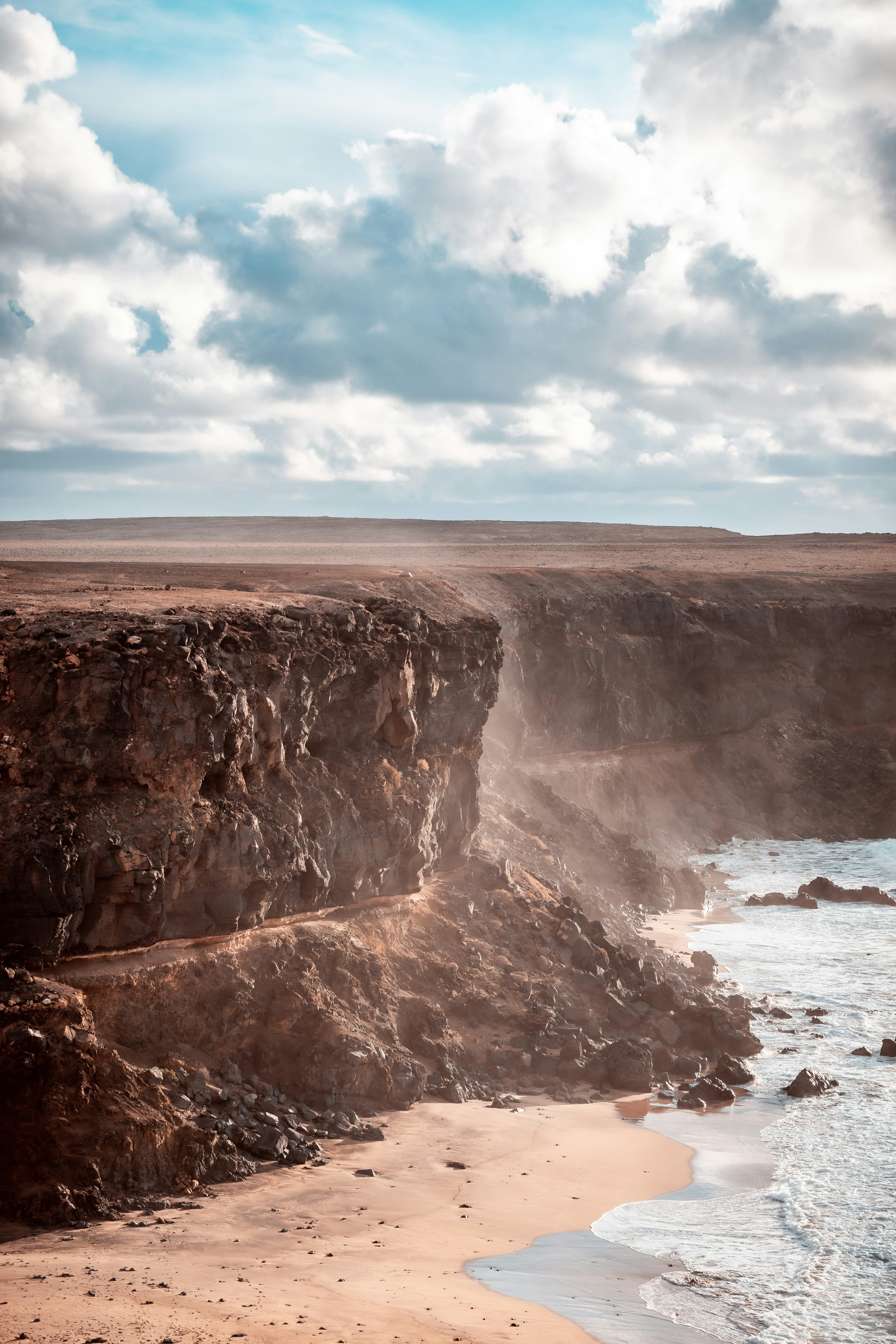 Towering volcanic cliff face with Atlantic sea spray rising from the crashing waves below